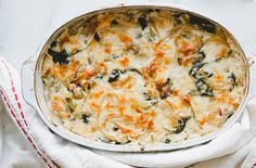 a casserole dish with cheese and spinach in it on a white cloth