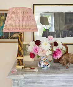 a table with a lamp, vase and flowers on it in front of a mirror