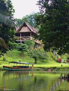 a boat is on the water in front of a small hut with thatched roof