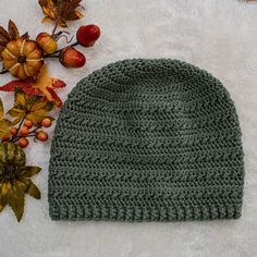 a green knitted hat sitting on top of a white rug next to autumn leaves