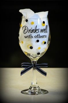 a wine glass with polka dots on it that says drinks well with others, and has a bow at the bottom