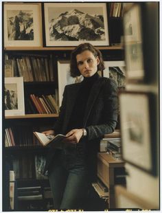 a woman standing in front of a bookshelf with many pictures on the wall