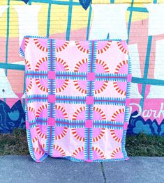 a pink and blue quilt sitting on top of a sidewalk next to a graffiti covered wall