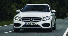 the front end of a white mercedes c - class driving on a road with trees in the background