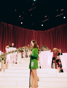 a woman in a green dress is standing on stage with an instrument and choir behind her