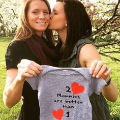 two women kissing each other while holding up a t - shirt that says 2 mommies are better than 1