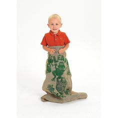 a young boy standing on top of a bag filled with sand and wearing an orange shirt