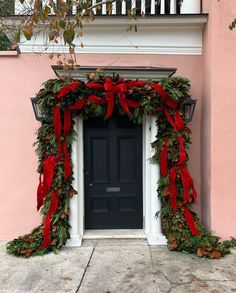 a black door with red bows and greenery on the outside, next to a pink building