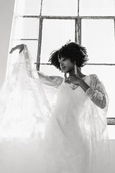 a black and white photo of a woman in front of a window wearing a wedding dress