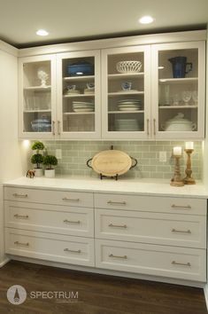 a kitchen with white cabinets and glass front cupboards on the counter top is lit by two lamps