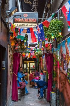 people sitting at tables in an alleyway with flags hanging from the ceiling and paintings on the walls