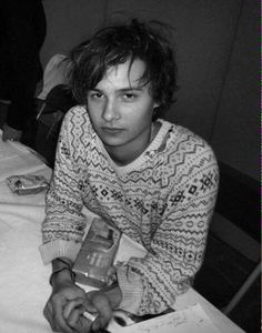 a young man sitting at a table holding a cell phone