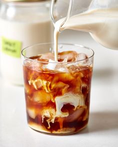 a pitcher pouring milk into a glass filled with ice