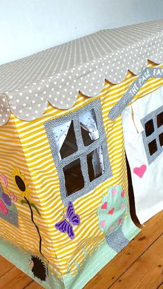 a doll house made out of fabric with windows and flowers on the front, sitting on a wooden floor