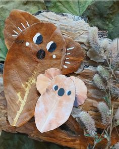 two leaf shaped animals sitting on top of a wooden log next to plants and leaves