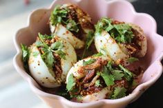 some food is in a pink bowl on a white table top and there are herbs sprinkled all over it