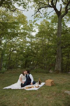 a bride and groom are sitting on a blanket in the woods, sharing a picnic