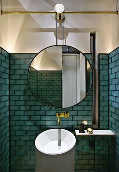 a bathroom with green tiles and a round mirror above the sink, along with a gold faucet