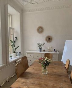 a wooden table sitting in front of a window next to a vase with flowers on it