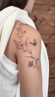 a woman with a butterfly tattoo on her upper arm and behind her shoulder is a branch with butterflies