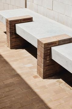 two concrete benches sitting next to each other on a brick floored area near a wall