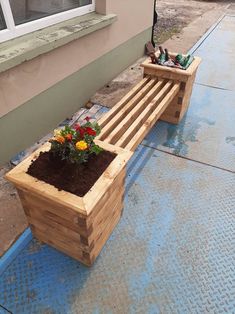 a wooden bench sitting on the side of a building next to a flower pot filled with flowers