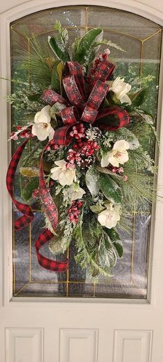 a christmas wreath with flowers and greenery hanging on a front door glass paneled window