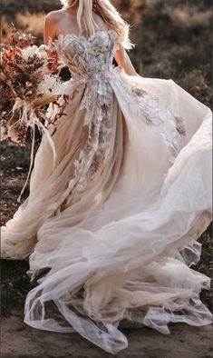 a woman in a dress with flowers on her head is walking through the grass and holding a bouquet