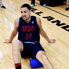 a basketball player sitting on the floor with his hands out and feet up in the air