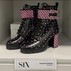 a pair of black boots with pink and white polka dots on them sitting on top of a shelf