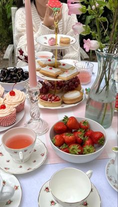 a table topped with plates and cups filled with food next to a vase full of strawberries