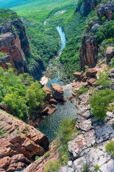 a river running through a lush green valley surrounded by rocky cliffs and trees in the distance