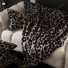 a leopard print throw blanket sitting on top of a white couch next to two pillows