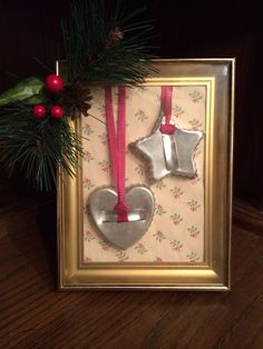 two ornaments are hanging in a frame on the floor next to a christmas tree branch