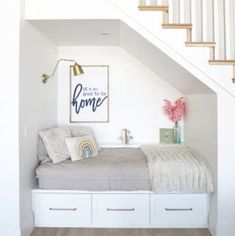 a bed sitting under a stair case next to a white staircase leading up to a second floor