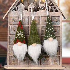 three christmas gnome ornaments hanging from a wooden house