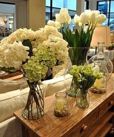 vases filled with white flowers sitting on top of a wooden table in front of a couch