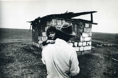 black and white photograph of a woman leaning against a brick building with a cowboy hat on her head