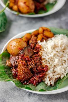 two plates filled with rice, meat and vegetables on top of leafy green leaves