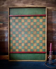 a green and yellow checkered wall hanging next to a purple candle