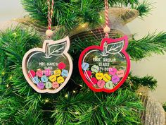 two christmas ornaments hanging from a tree with ribbons on it's sides, one has an apple shaped ornament and the other is made out of wood