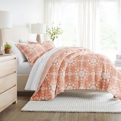 a bed with an orange and white comforter in a bedroom next to a window