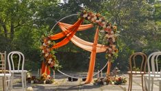 an outdoor wedding set up with orange and white draping, flowers and chairs