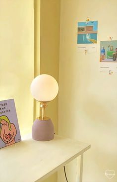 a lamp sitting on top of a white table next to a book and a window