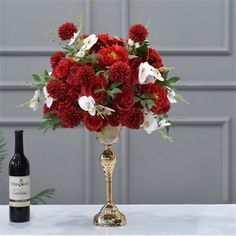 a vase with red and white flowers next to a bottle of wine on a table