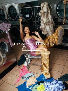 a woman sitting on top of a chair next to a pile of clothes in front of a washer