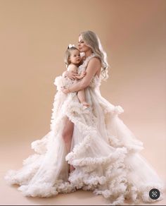 a woman holding a baby in her arms and wearing a dress with ruffles on it