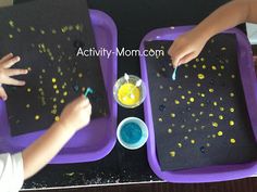 two children are sitting at a table with black trays and yellow dots on them