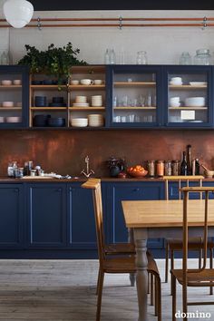 a kitchen with blue cabinets and wooden table in the foreground is a dining room