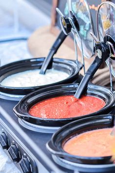 three different types of sauces in black bowls on a stove top with tongs